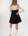 Back view of Black Hem Mini Dress with smocked bodice and bubble skirt, styled with mesh sleeves and white boots for a modern flair.