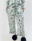 Close-up of Heritage Holiday Toile Green Pajama Set pants with green holiday motifs, ruffle trim, and striped ribbon drawstring for adjustable fit.