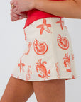 Sally Red Seashell Printed Mini Skirt in coastal-chic poppy red with vibrant shell motifs, styled with a red top for a beach-ready look.