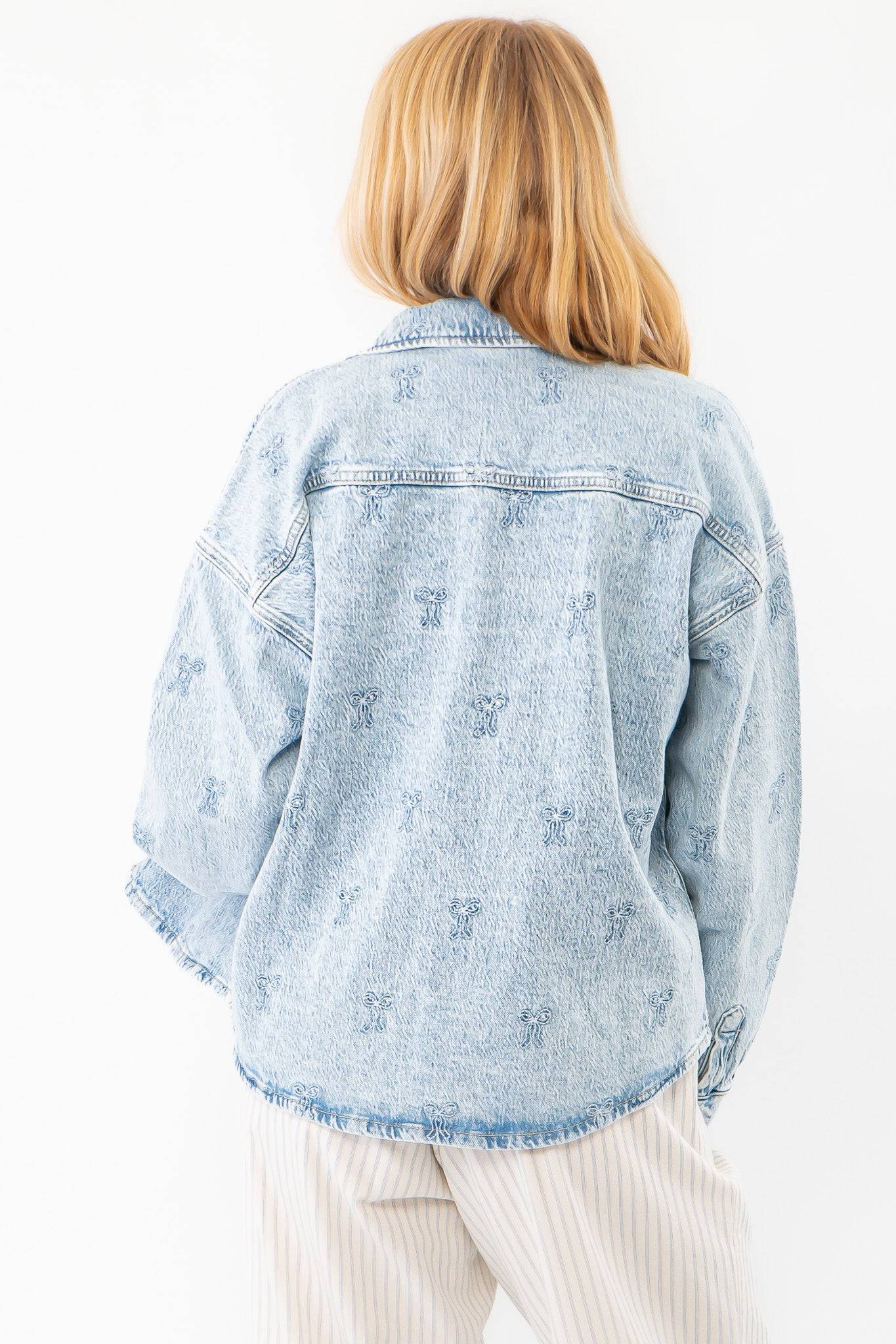 Back view of the Chill Charm Bow Detail Denim Jacket showcasing embroidered bow accents on a light-wash denim fabric with a relaxed fit.