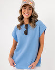 Front view of Camila Powder Blue Knit Top paired with white pants and a cap, highlighting its soft knit texture and flattering round neckline.