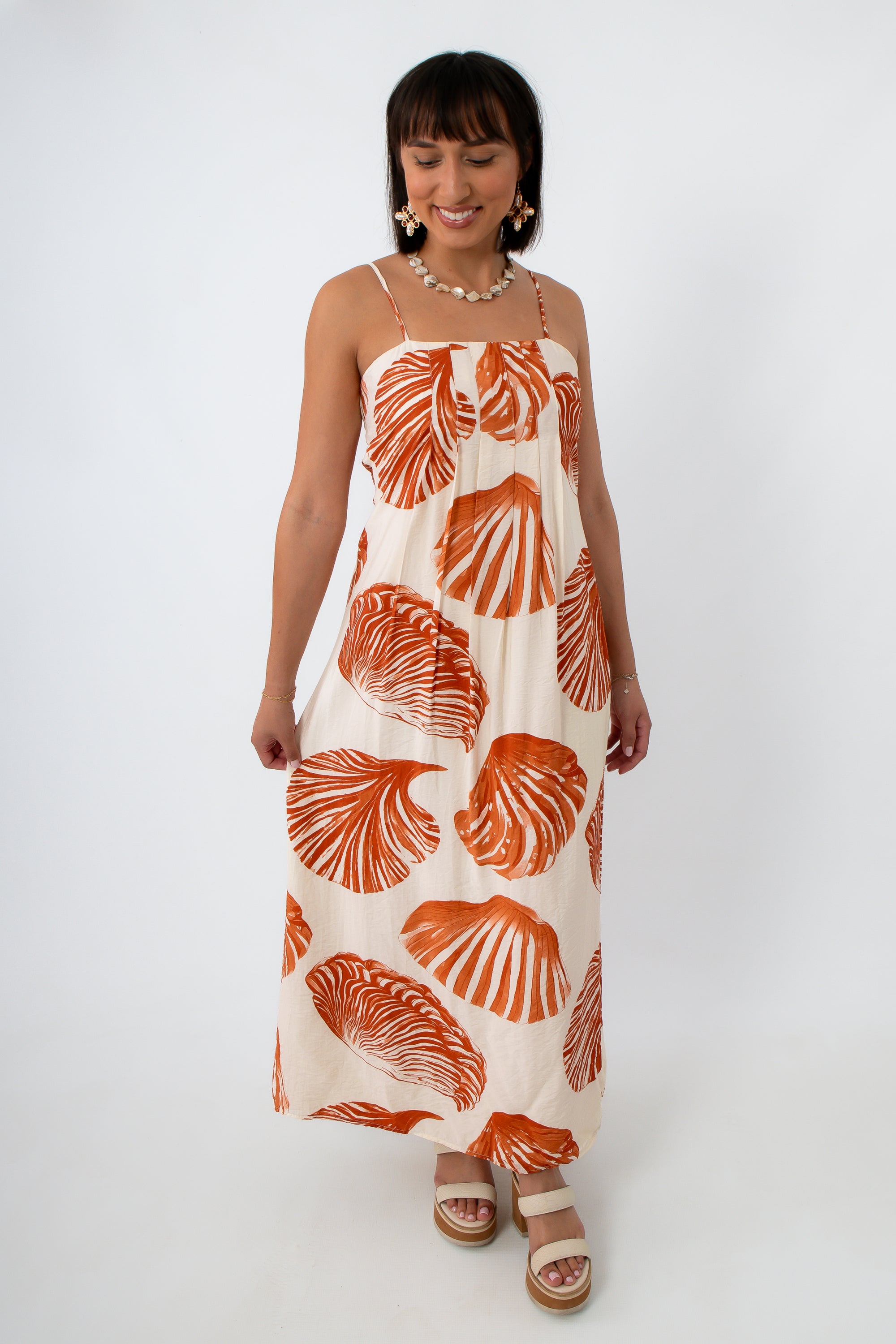 Side view of woman in orange shell print maxi dress with shell jewelry
