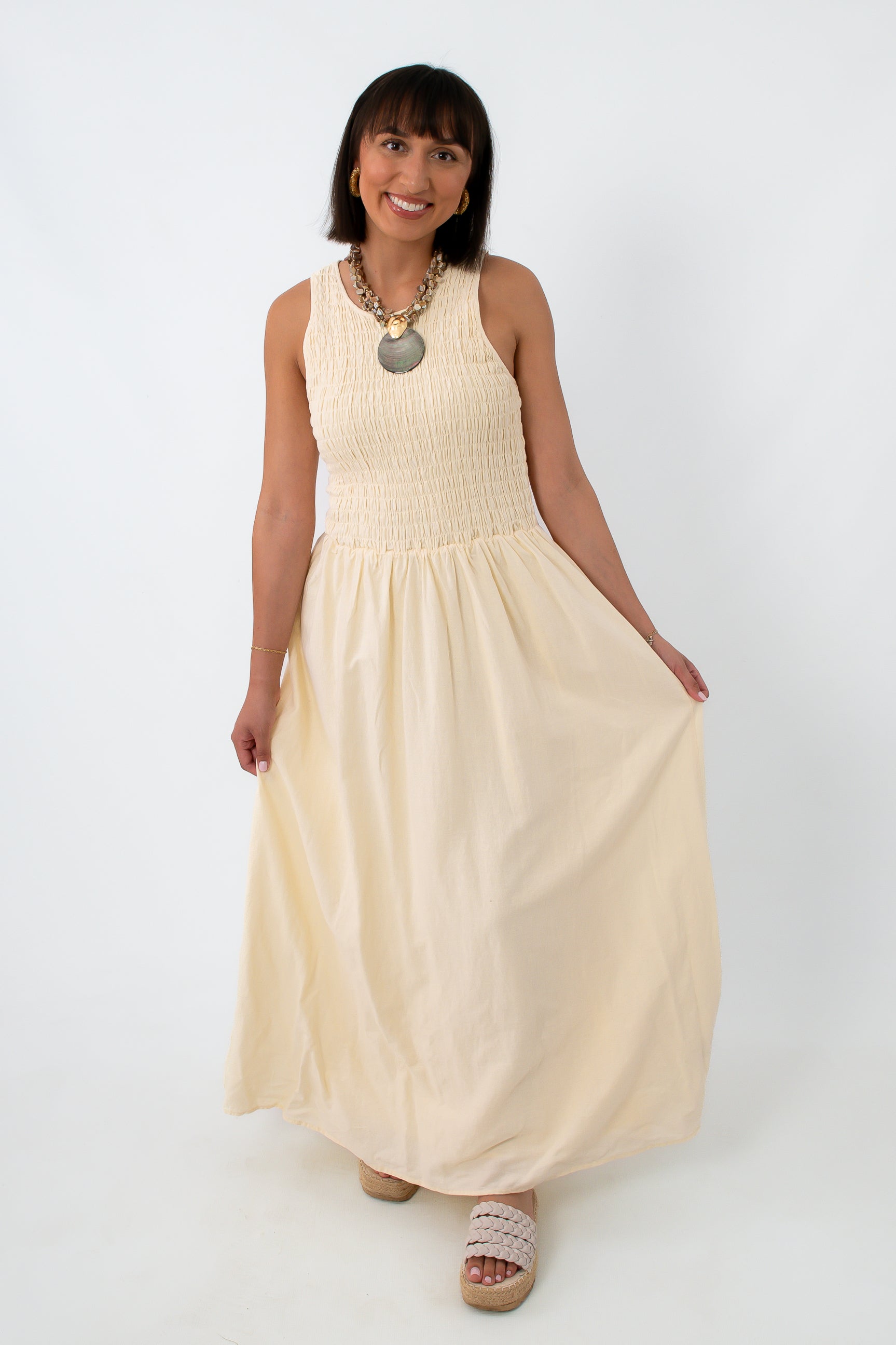 Woman in cream maxi dress with smocked bodice and open keyhole back, standing against white background