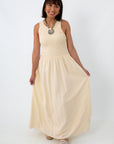 Woman in cream maxi dress with smocked bodice and open keyhole back, standing against white background