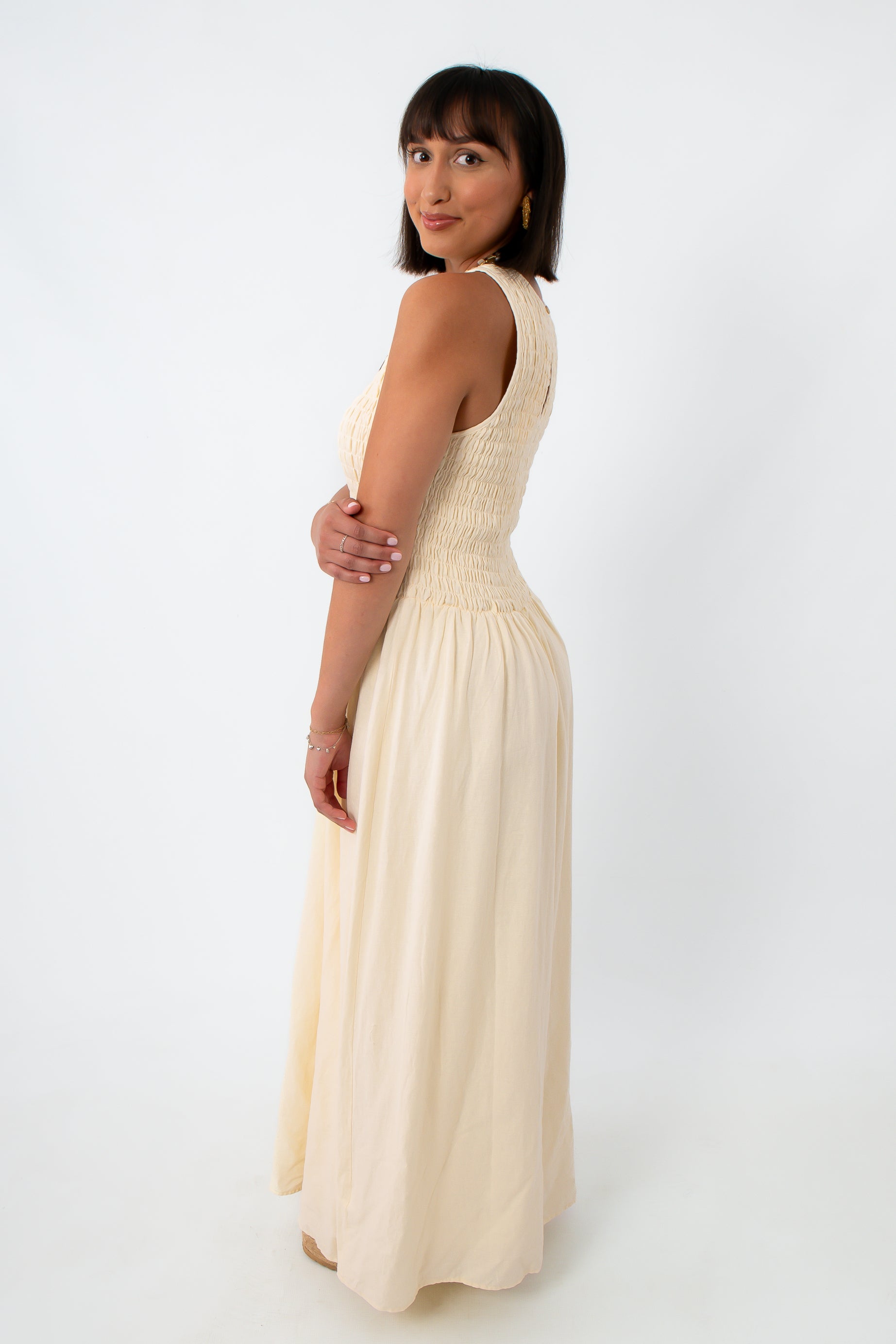 Back view of woman in cream maxi dress with keyhole back detail, standing with hand on hip