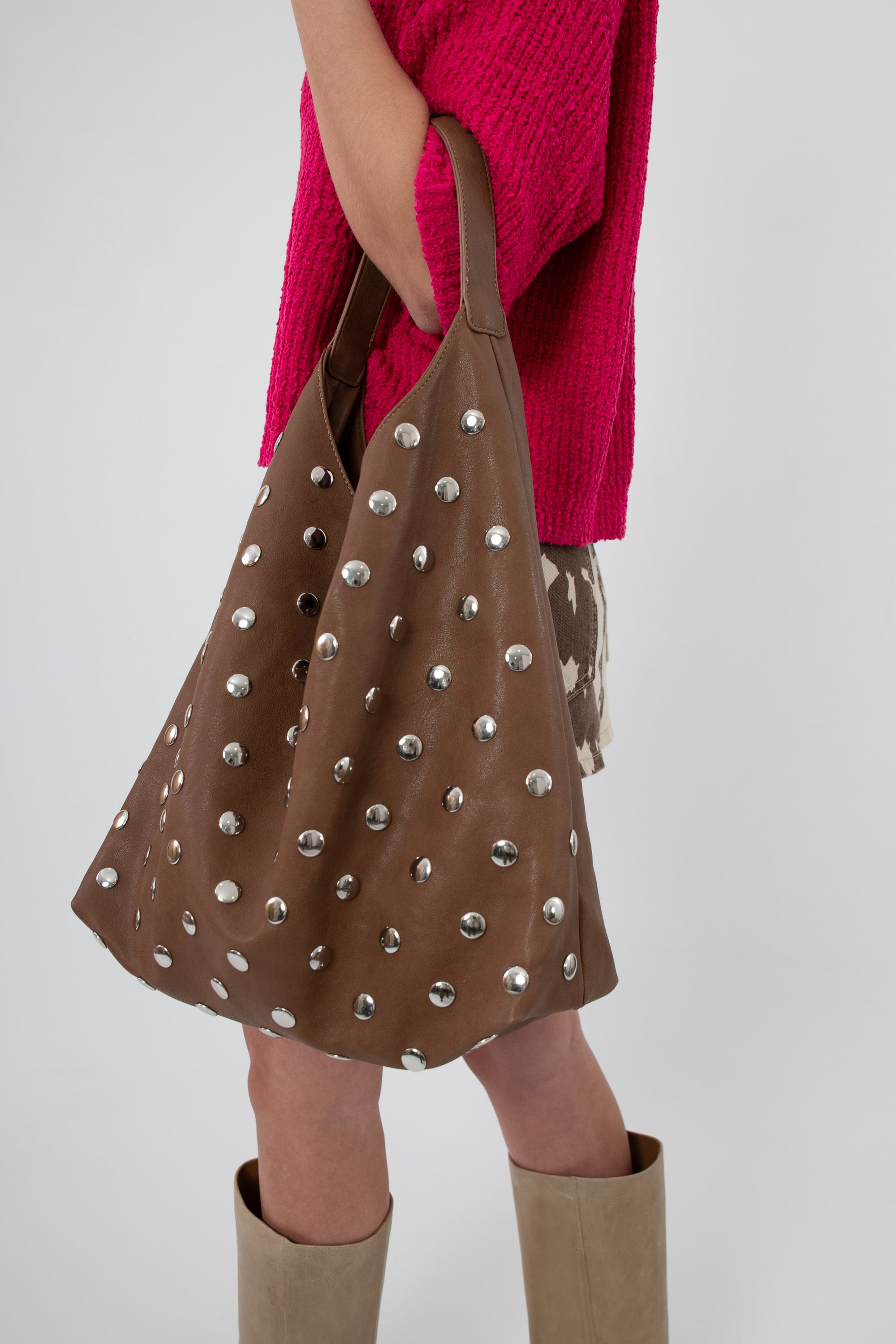 Model holding brown studded slouchy shoulder bag with pink top
