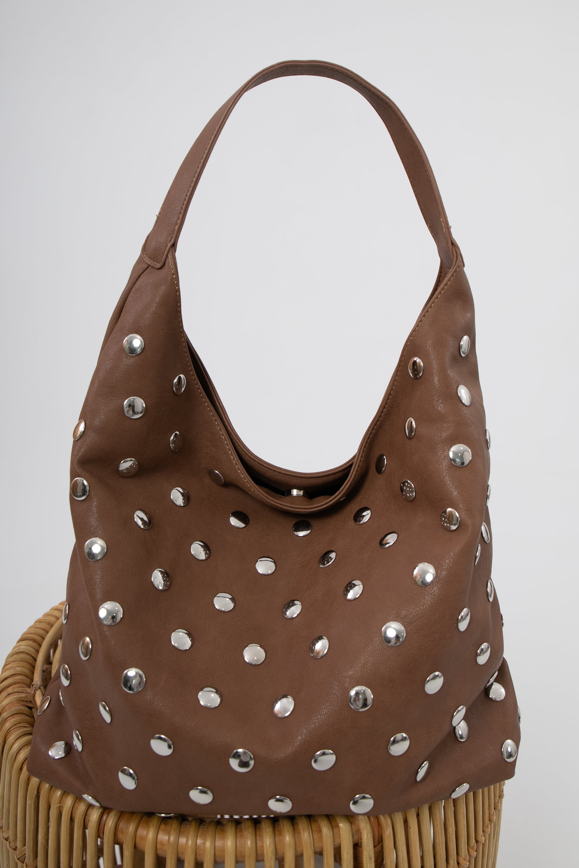 Brown studded slouchy shoulder bag on a wicker chair