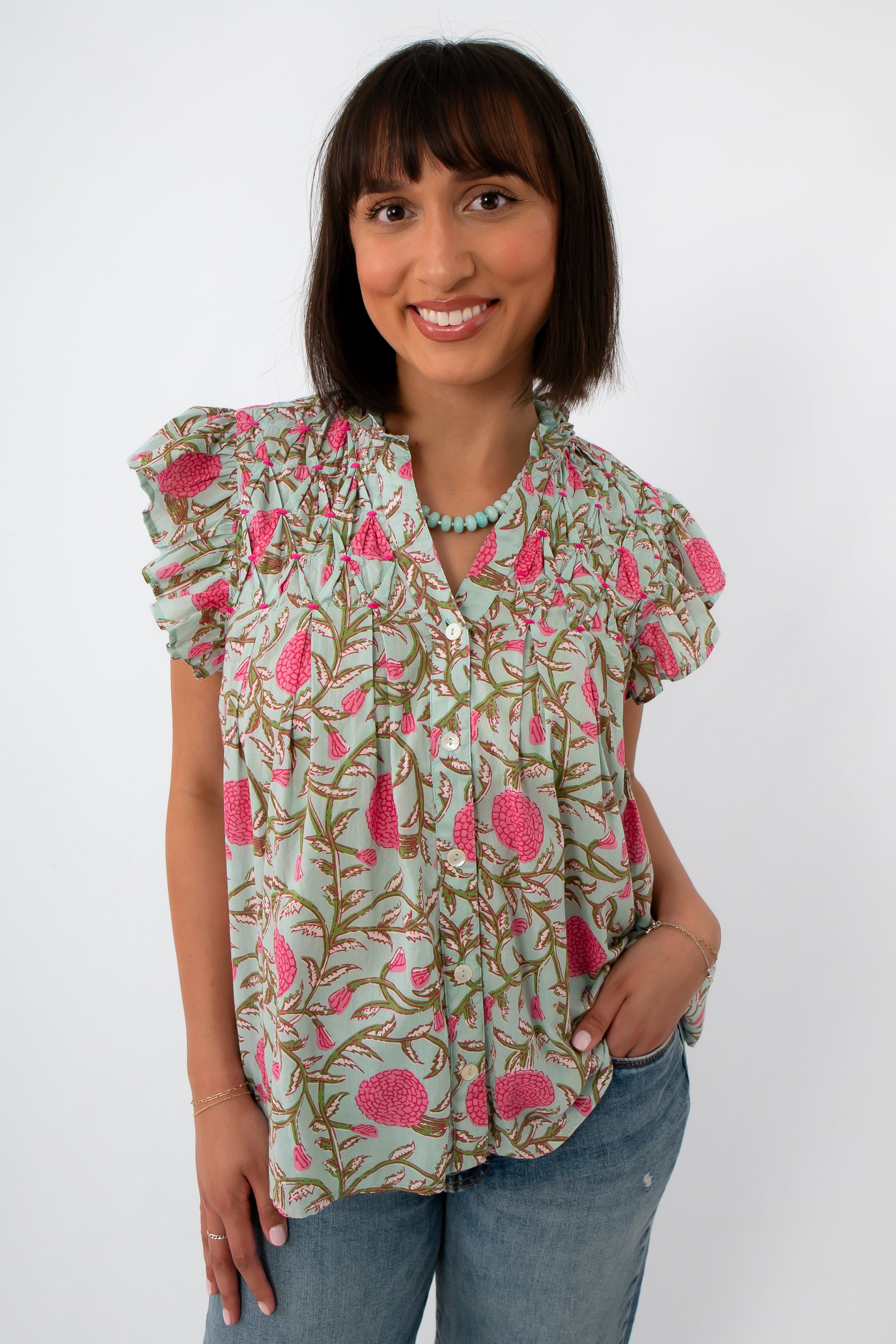 Woman wearing mint floral flutter sleeve blouse with ruffled shoulders and button front