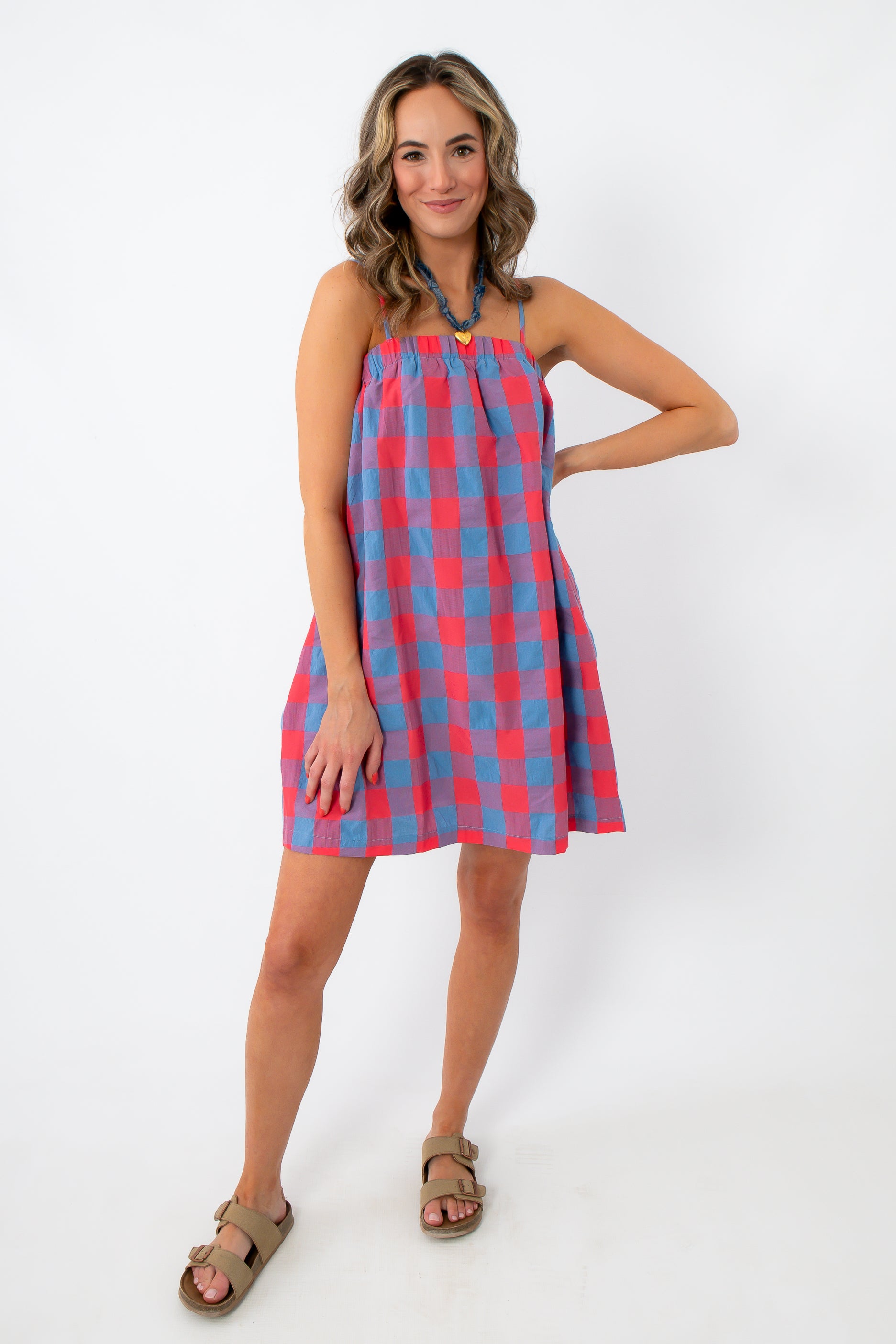 Close-up of woman smiling in a red and blue plaid mini dress with adjustable straps and pockets, white background