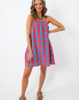 Close-up of woman smiling in a red and blue plaid mini dress with adjustable straps and pockets, white background
