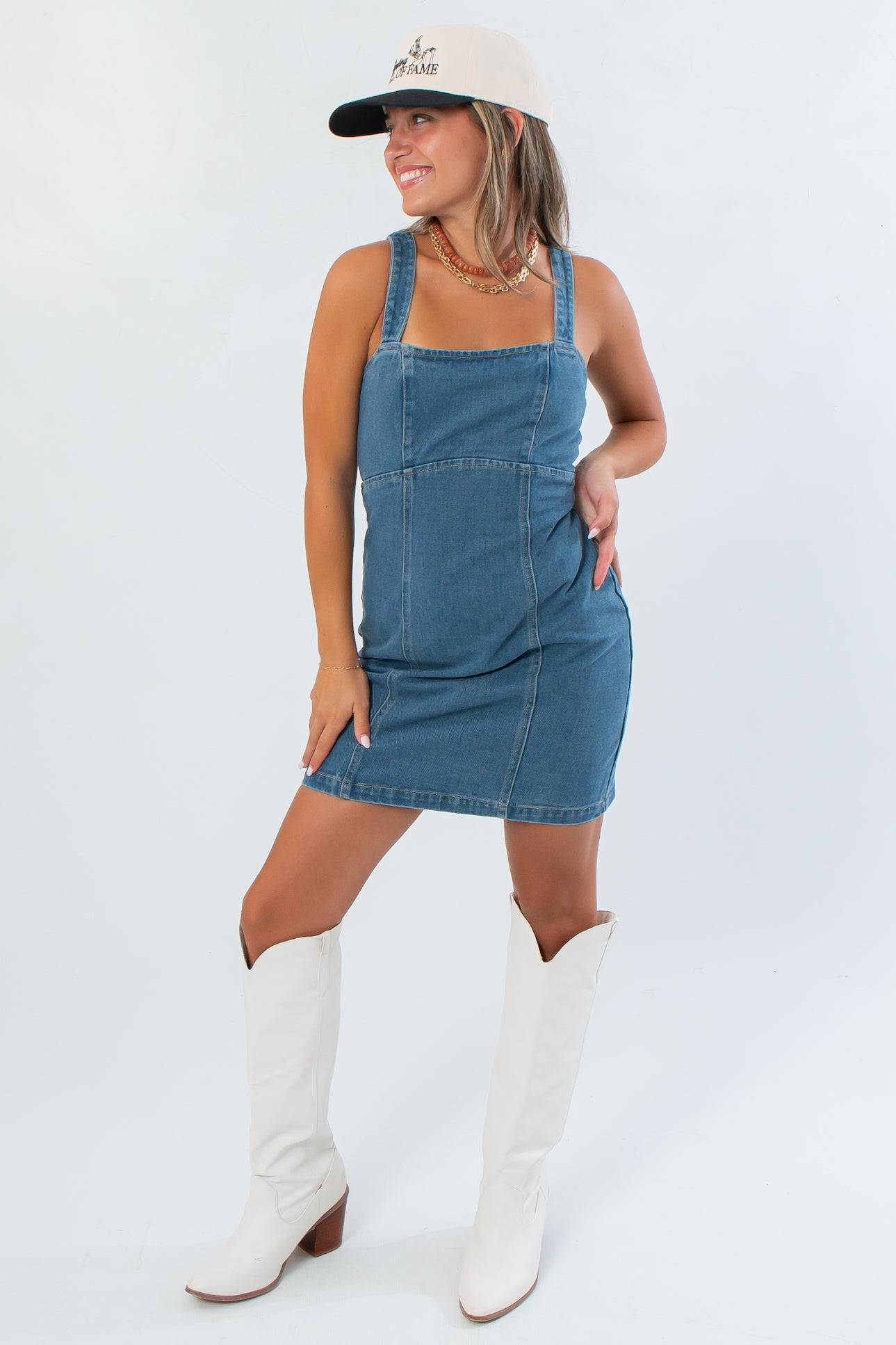 Karli Denim Corset Back Mini Dress in medium wash styled with white boots and a cap, perfect for a fitted gameday look.