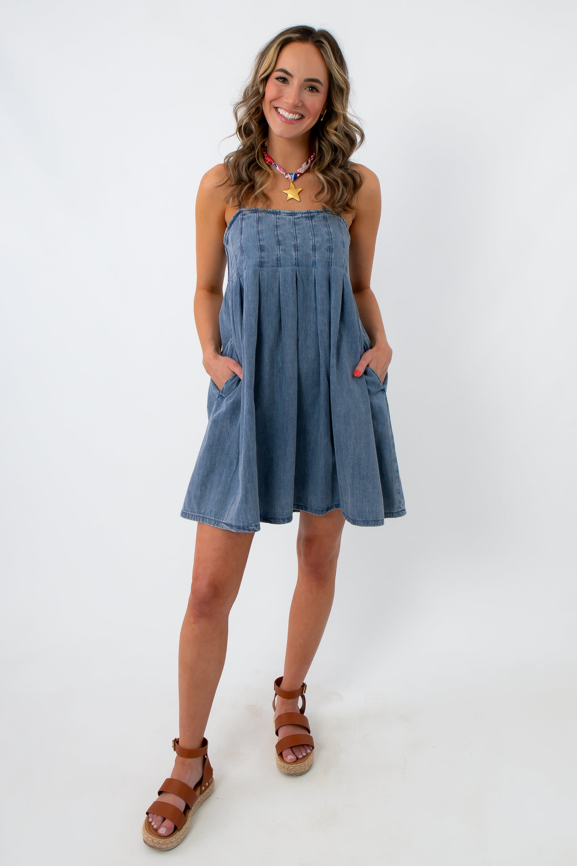 front view of woman smiling in denim dress with pockets and adjustable straps