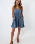 front view of woman smiling in denim dress with pockets and adjustable straps