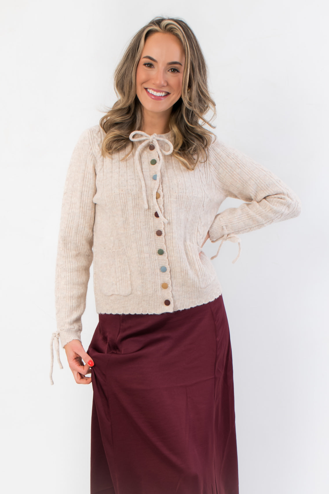 Juniper Multi Color Button Sweater – Beige ribbed cardigan with colorful buttons, self-tie bow at neckline, and front pockets for a cozy layered look.