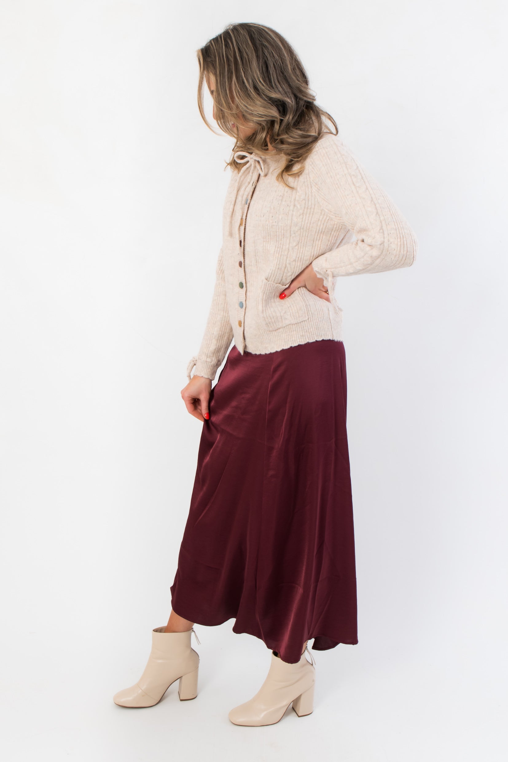 Juniper Multi Color Button Sweater – Side view of beige cardigan with ribbed texture and colorful buttons, styled with a burgundy skirt and cream boots.