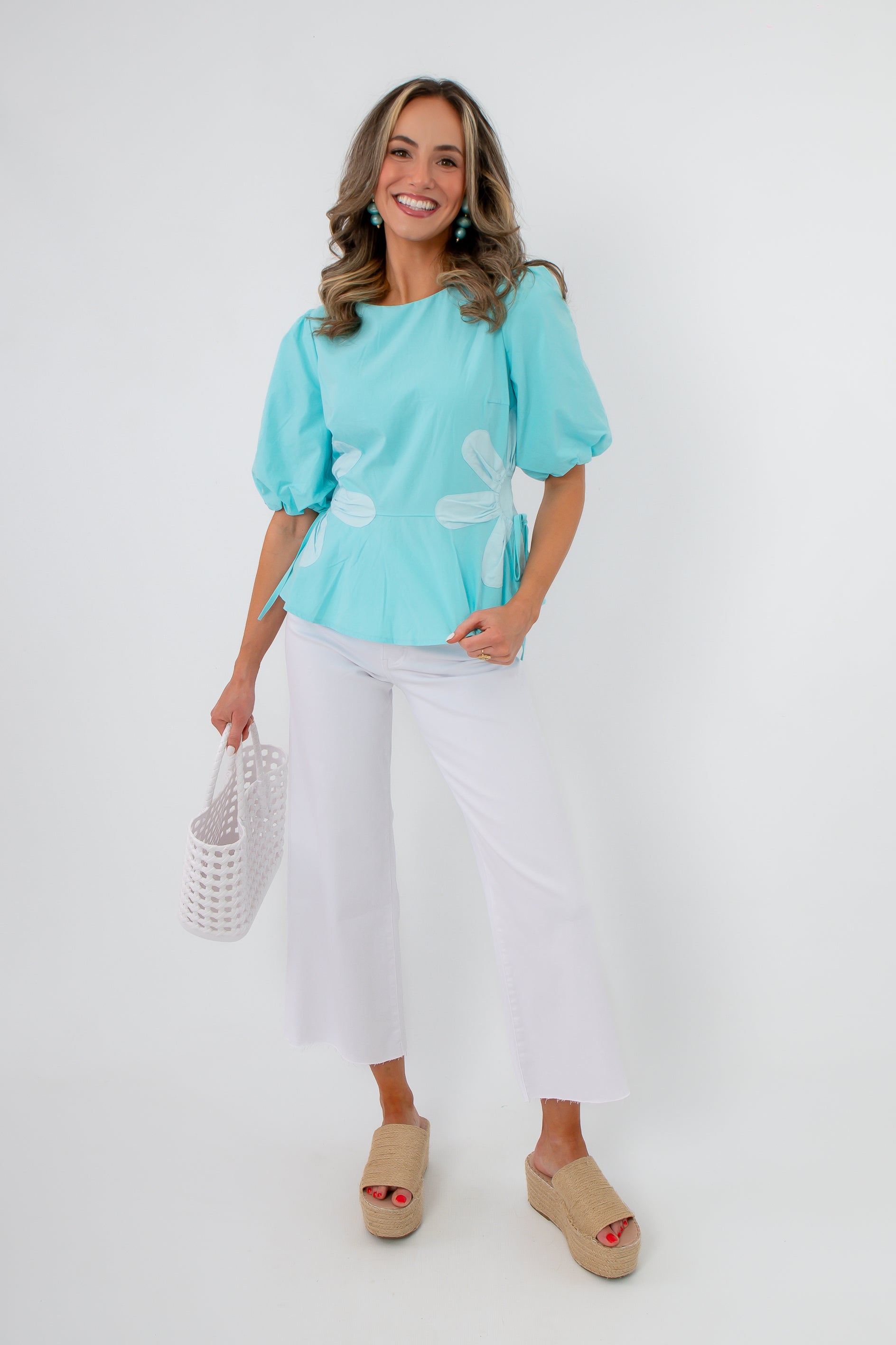 Model wearing retro daisy aqua blouse with white pants