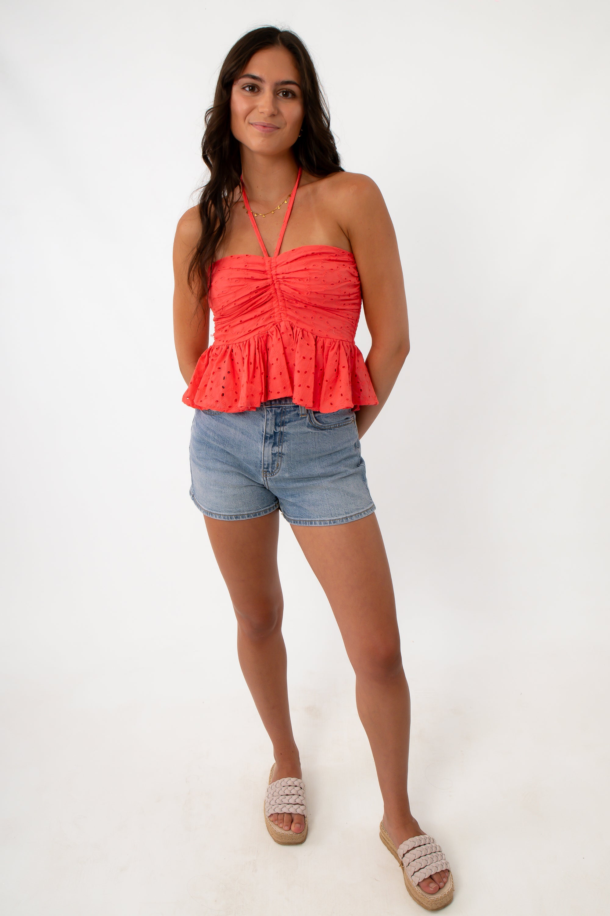 Woman wearing coral eyelet halter top with denim shorts, front view