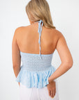 Side profile of woman wearing blue eyelet halter top with white pants