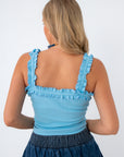 back view of woman in blue ruffle tank top and denim skirt