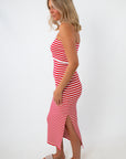 Back view of woman in red and white striped strapless knit midi dress with side slit, wearing beige platform sandals, standing against white background