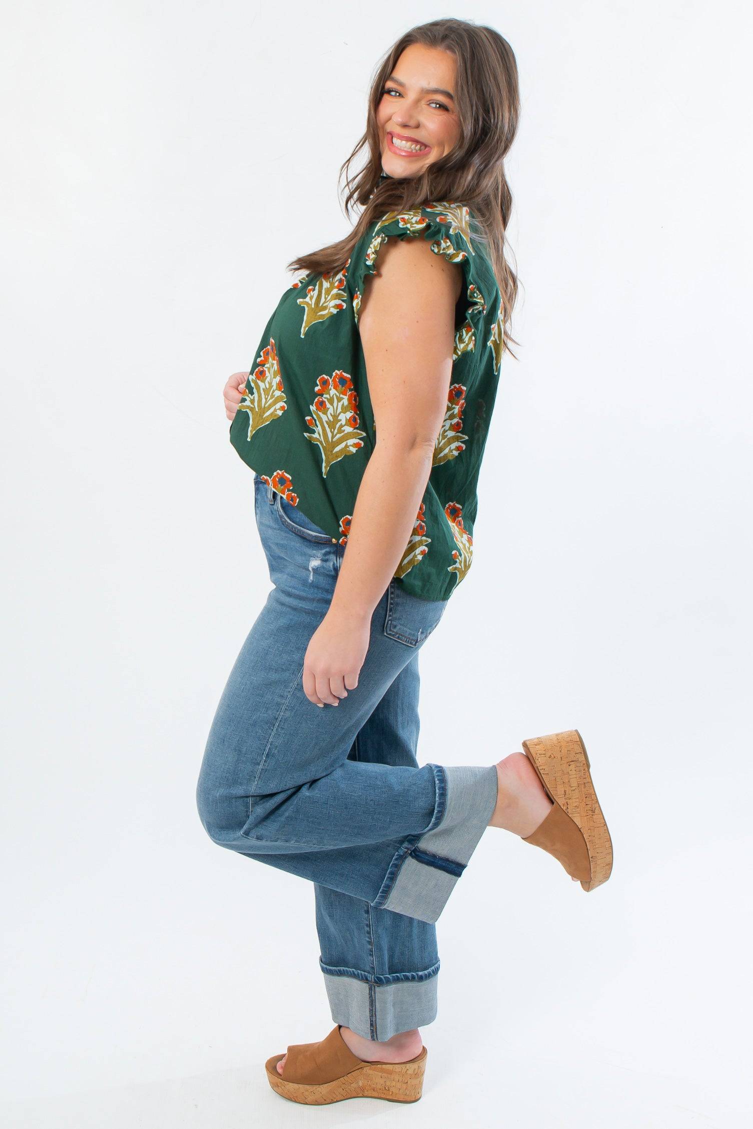 Side view of THML Dark Green Ruffle Sleeve Block Floral Print Blouse showcasing floral pattern and ruffle sleeves, paired with denim and wedges.