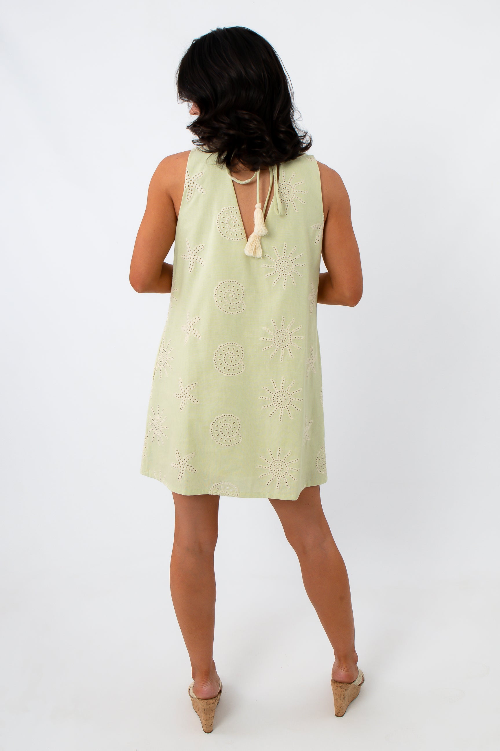 Woman in yellow embroidered sundress with shell necklace, side pose