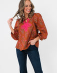 Carmen Rust Floral Embroidered Blouse with pink embroidery and balloon sleeves, styled with dark jeans for a chic fall outfit.