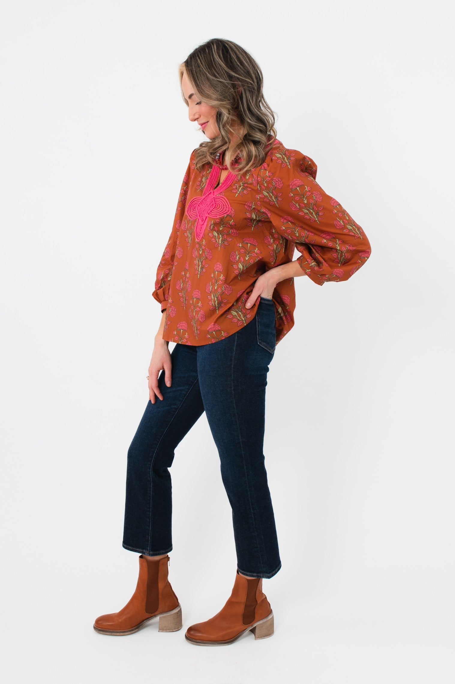 Side profile of Carmen Rust Floral Embroidered Blouse featuring pink floral embroidery and voluminous sleeves, styled with denim and boots.