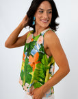 Woman wearing a vibrant tropical print sleeveless blouse with open back, smiling, holding a straw bag, white background
