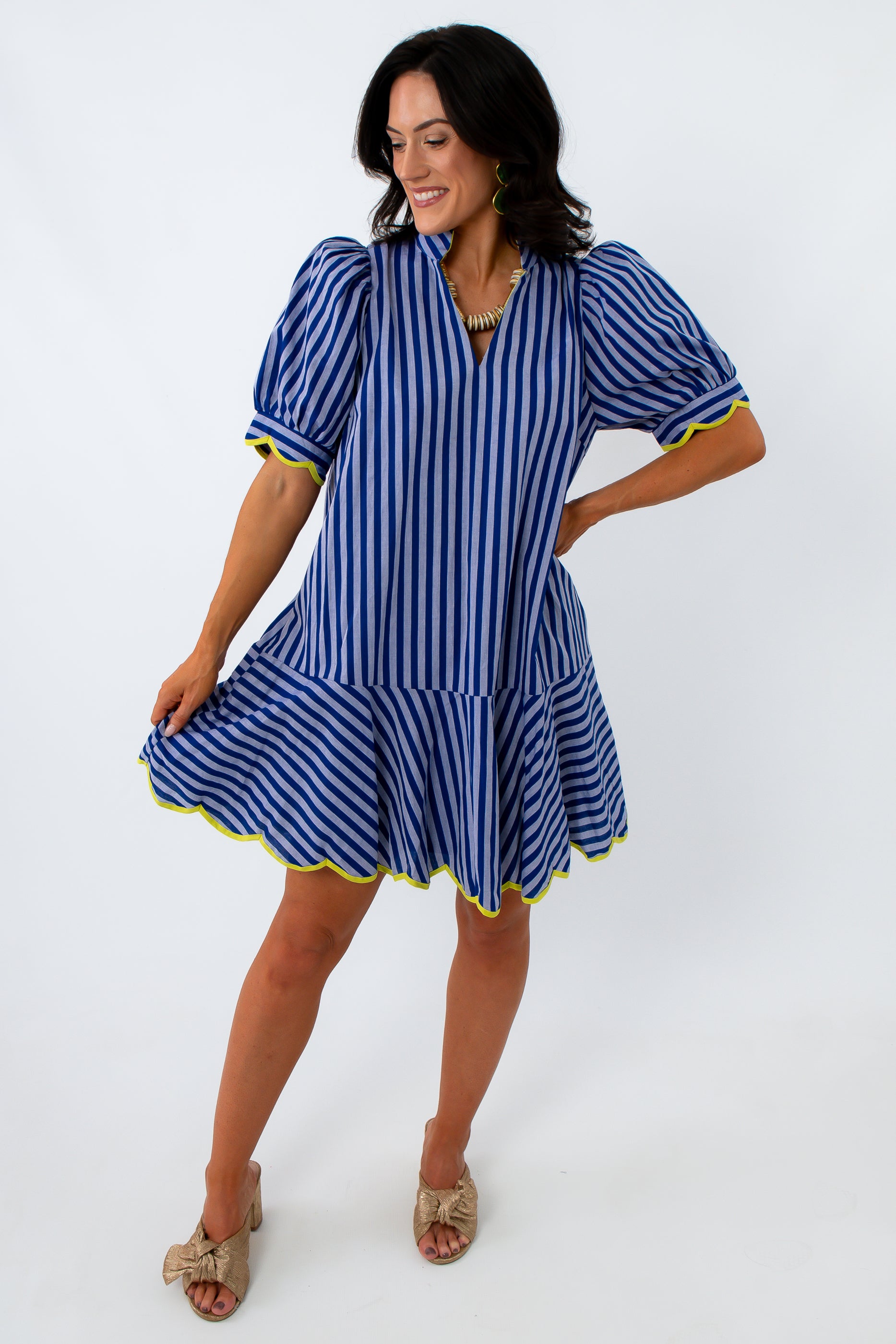 Side view of woman in blue striped dress with yellow trim, smiling, looking down