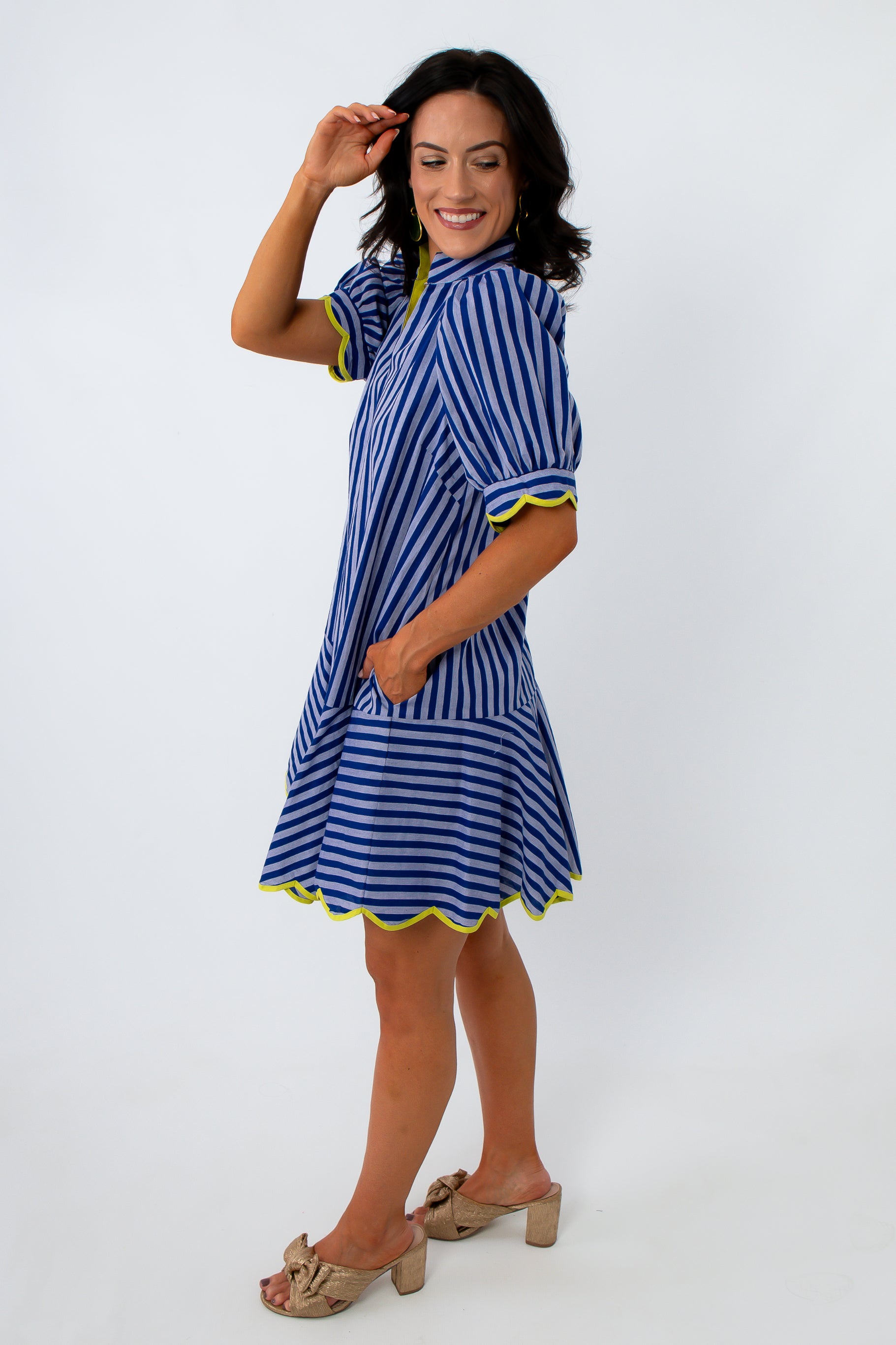 Woman in blue striped dress with yellow trim, smiling, posing against white background