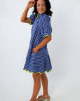 Woman in blue striped dress with yellow trim, smiling, posing against white background