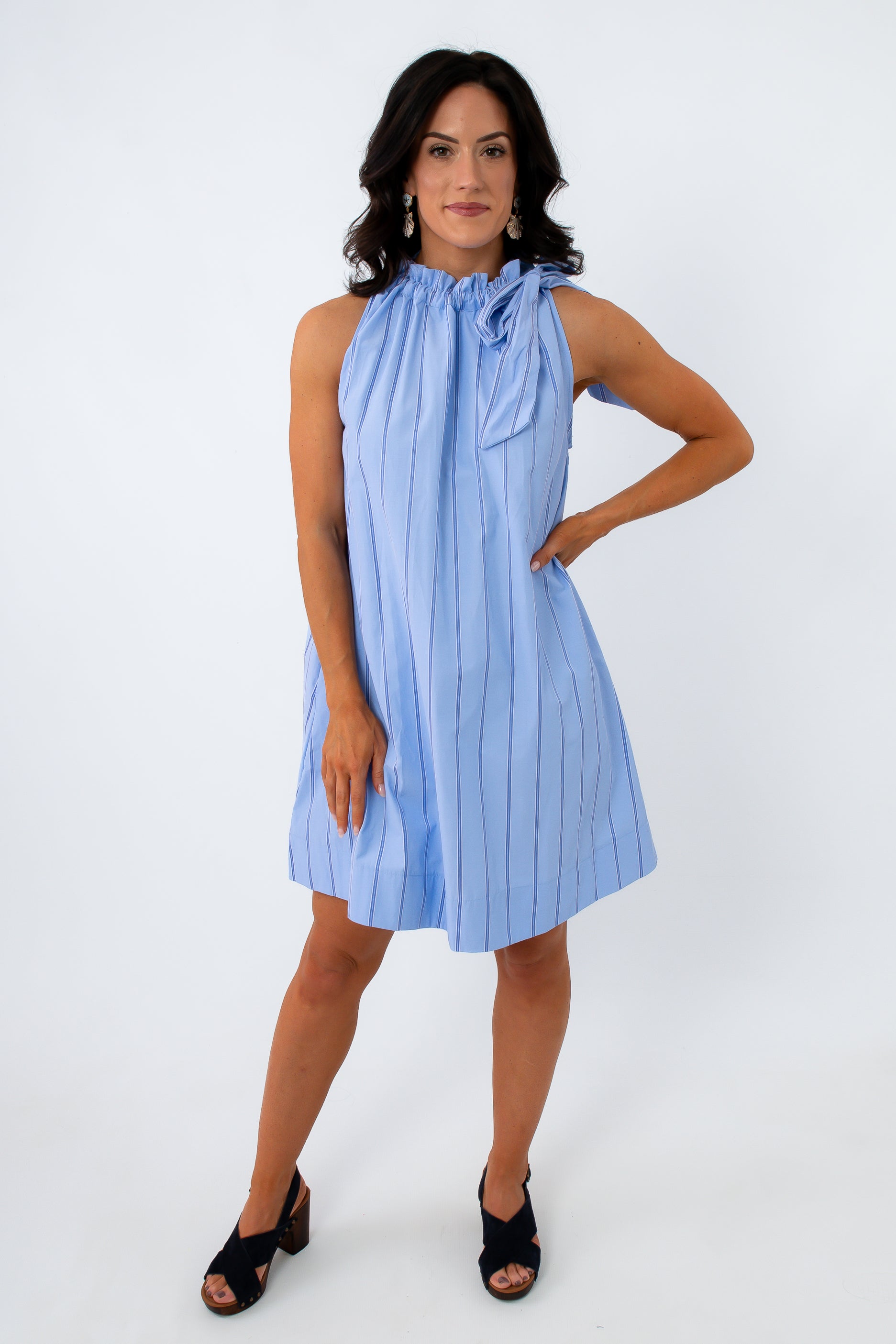 Full-body shot of woman in blue pinstripe dress with ruffled neckline and black heels, smiling
