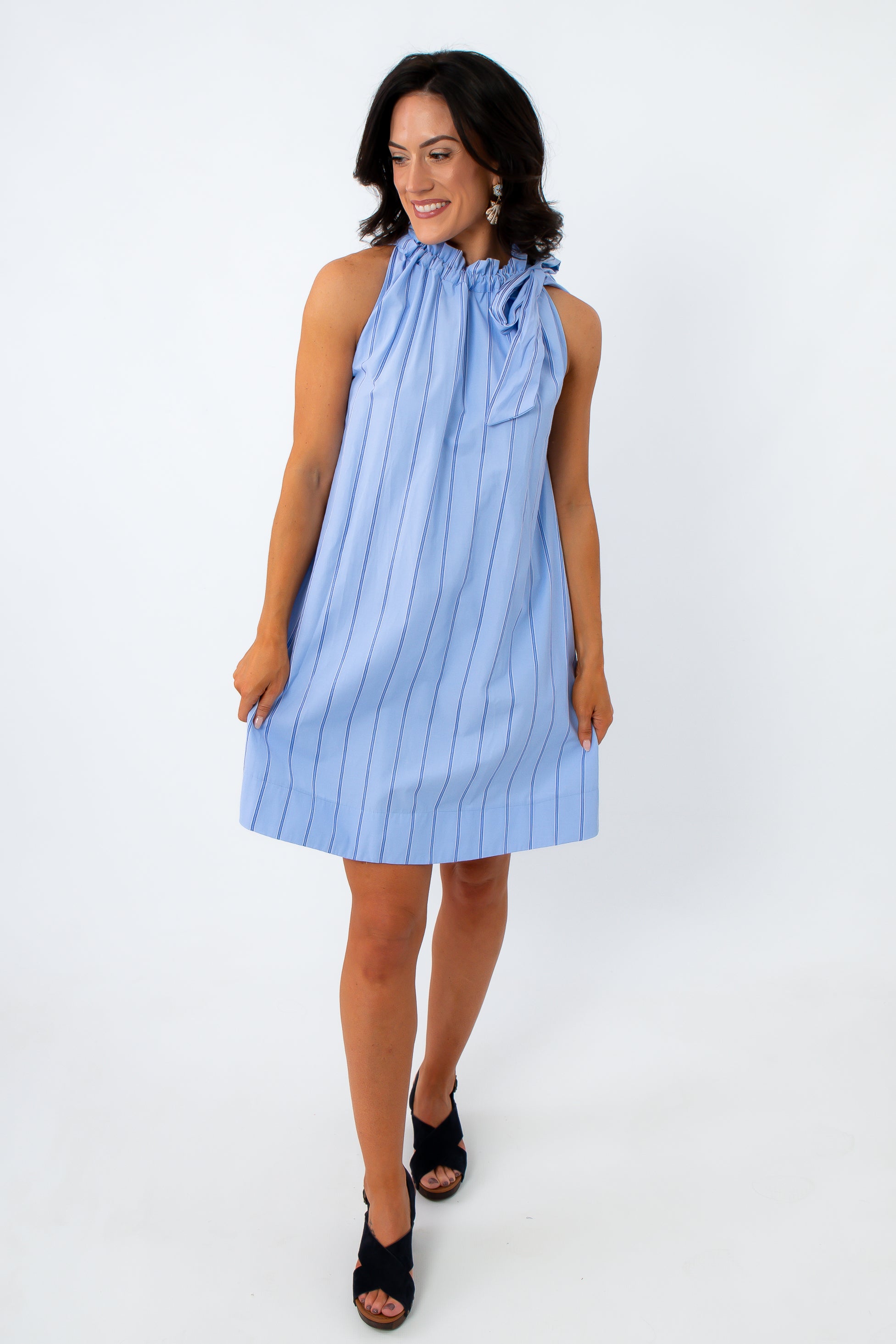 Woman in blue pinstripe dress with ruffled neckline and bow detail, standing against white background