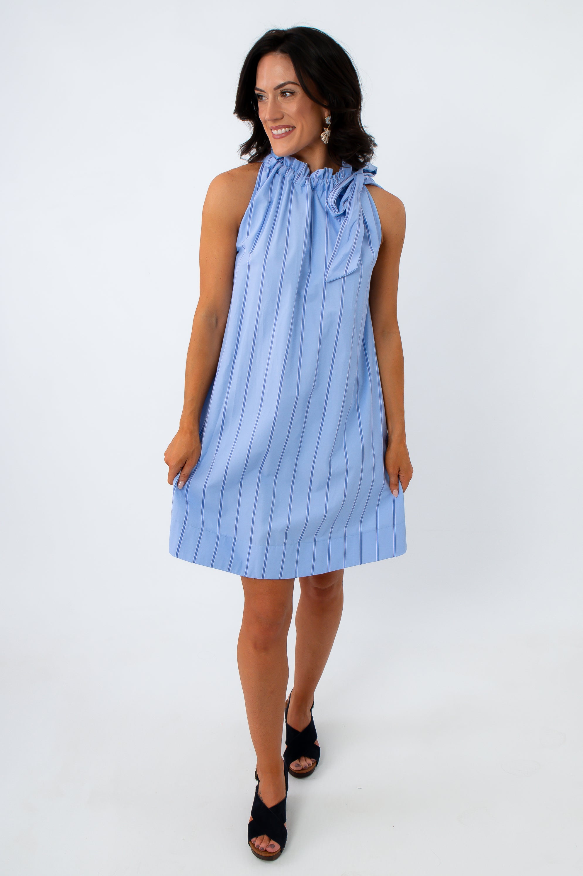Woman in blue pinstripe dress with ruffled neckline, standing with hand on hip, smiling