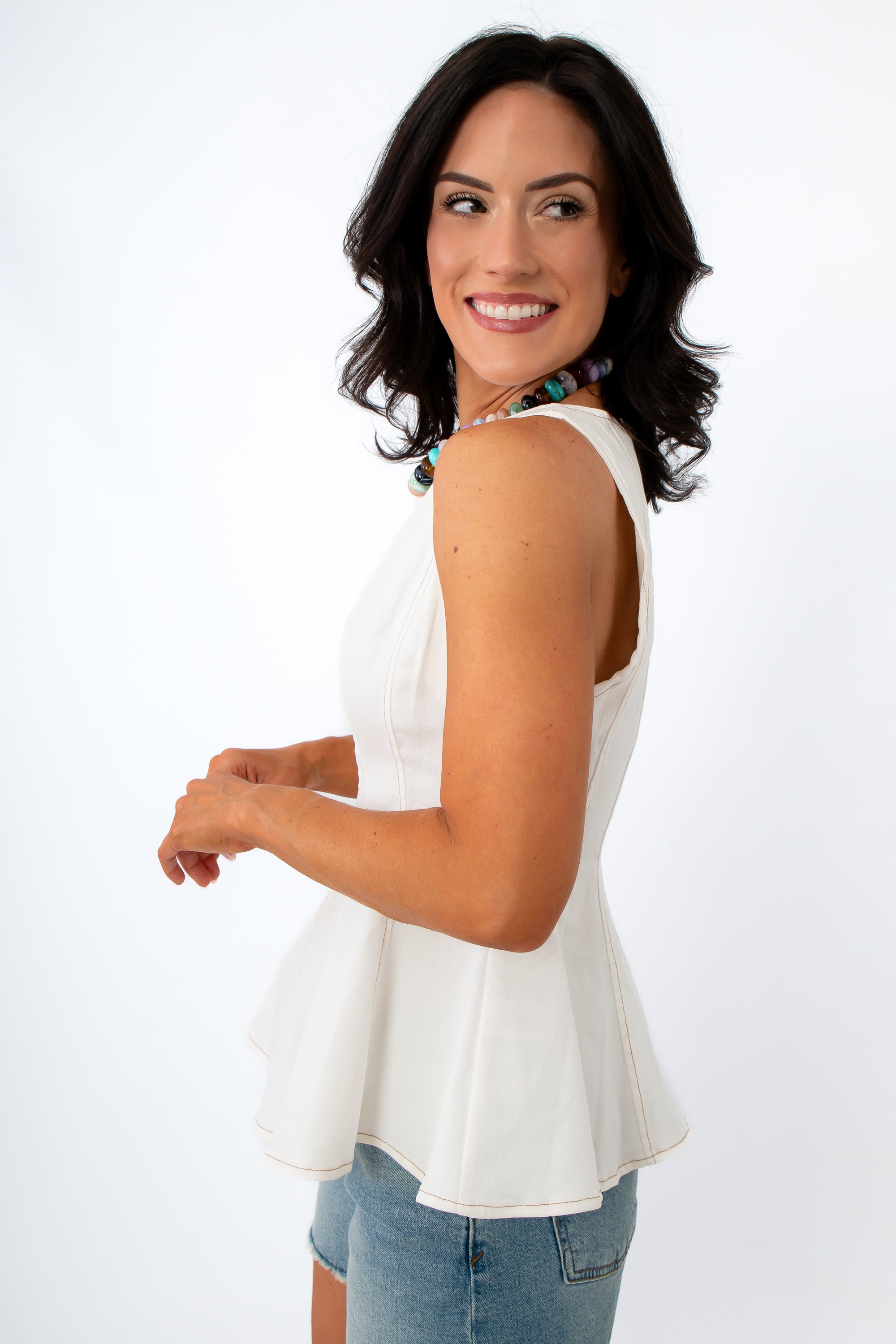 Women wearing white sleeveless peplum top with contrast stitching and a colorful beaded necklace