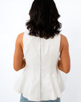 Back view of a woman wearing a sleeveless off-white top with a zipper and ruffled hem, paired with blue jeans