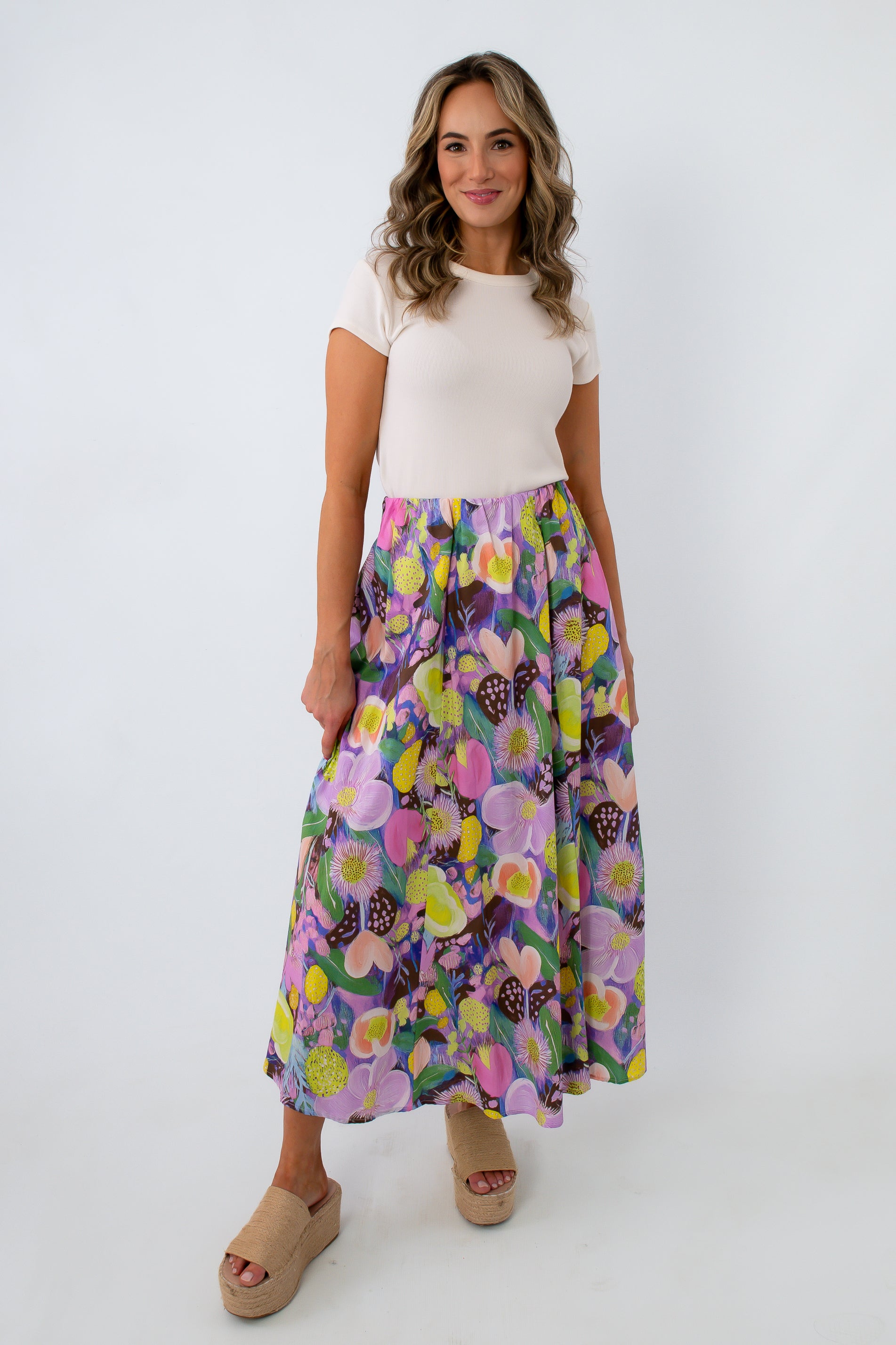Woman smiling in white top and vibrant floral maxi skirt