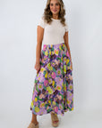 Woman smiling in white top and vibrant floral maxi skirt