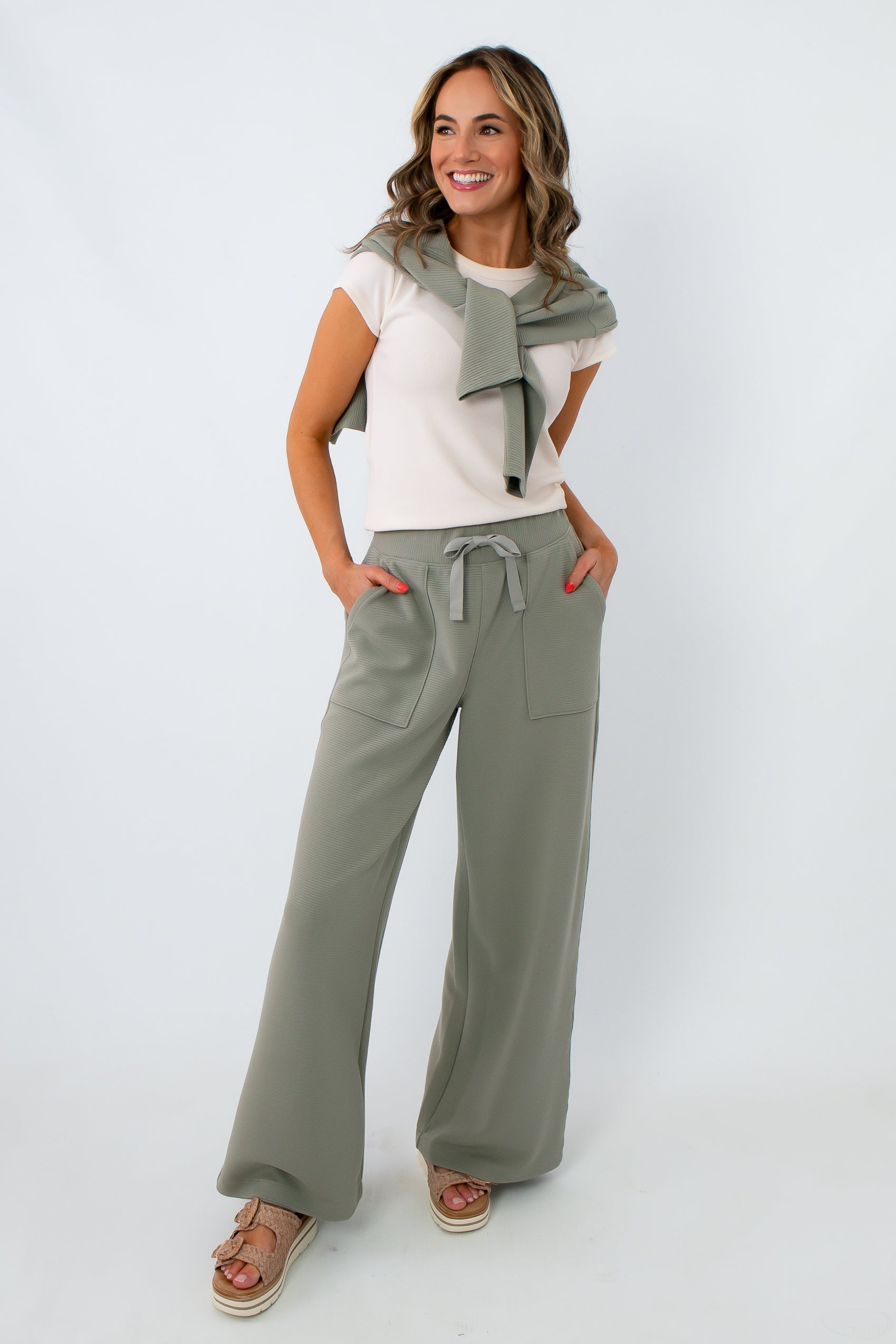 Full-body shot of woman in sage green lounge pants, beige sandals, and white top