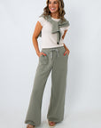 Full-body shot of woman in sage green lounge pants, beige sandals, and white top