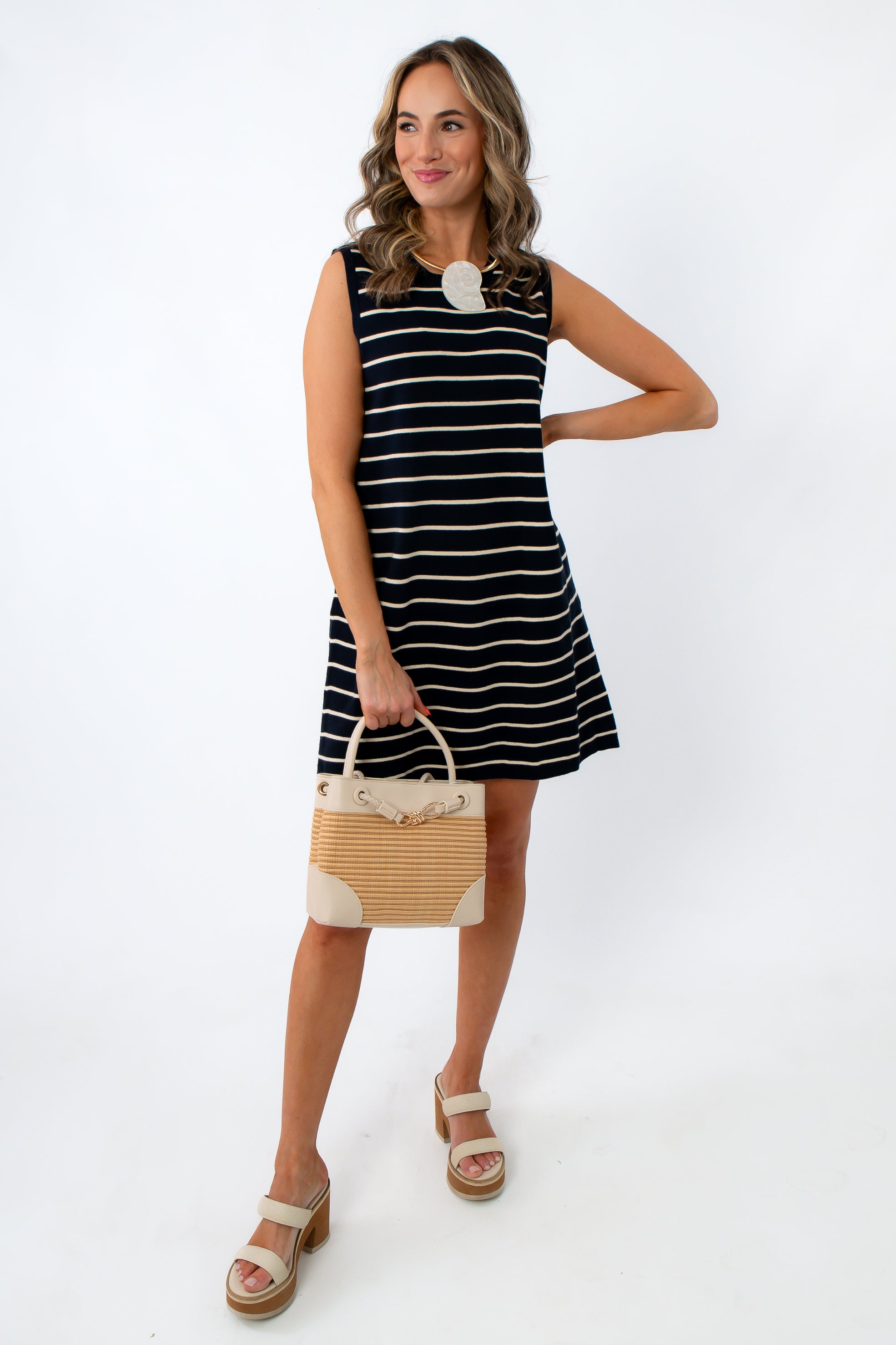 Woman in navy and white striped knit dress holding a beige handbag