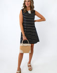 Woman in navy and white striped knit dress holding a beige handbag