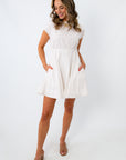 Side view of woman in white dress with pleated skirt and short sleeves, smiling