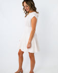 Woman in white dress with pleated skirt, standing sideways, smiling with eyes closed