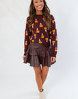 Candy Corn Lover Brown Sweater featuring playful candy corn graphics and premium knit fabric, styled with a tiered faux leather skirt.