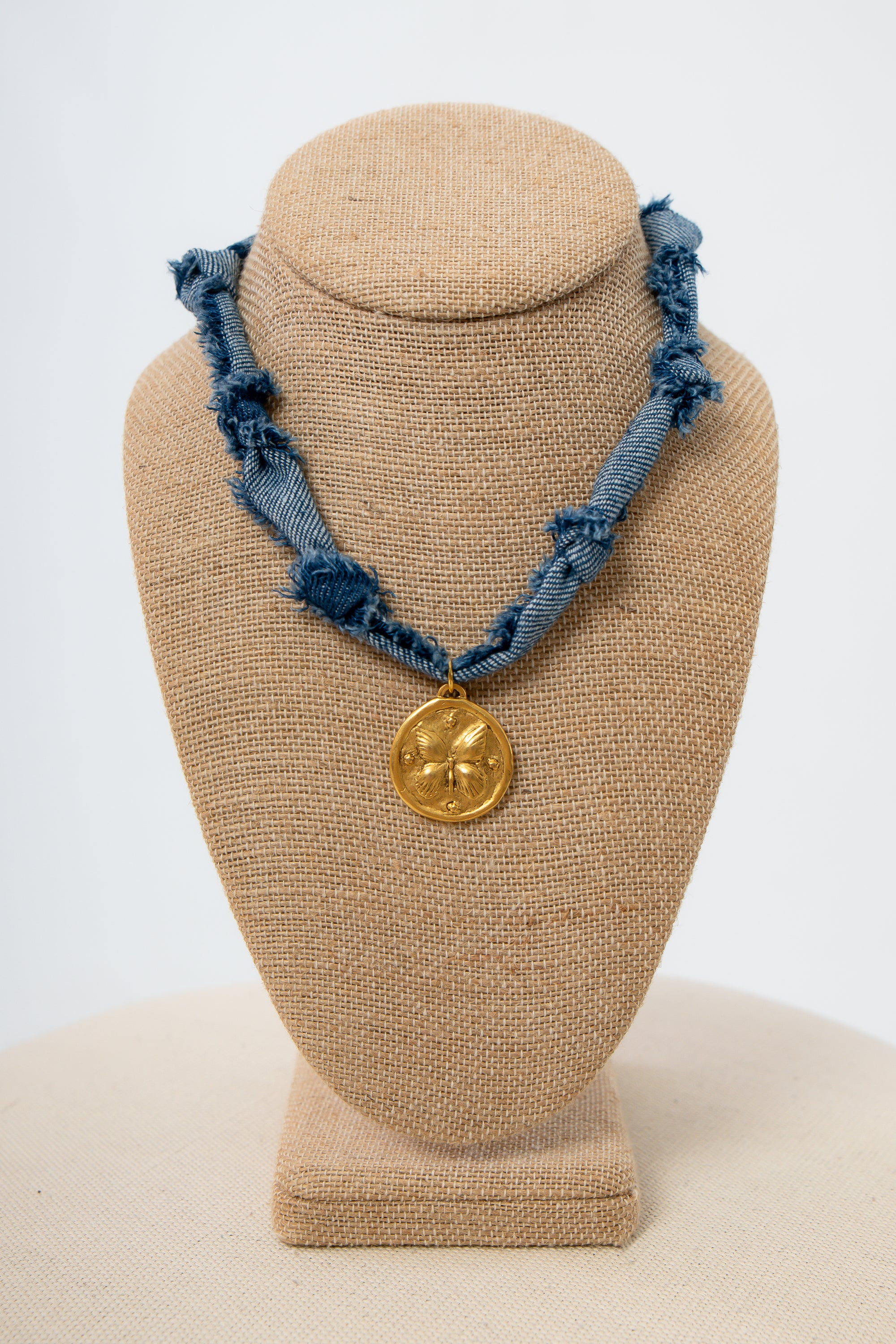 Denim necklace with a gold pendant on a beige bust against a white background