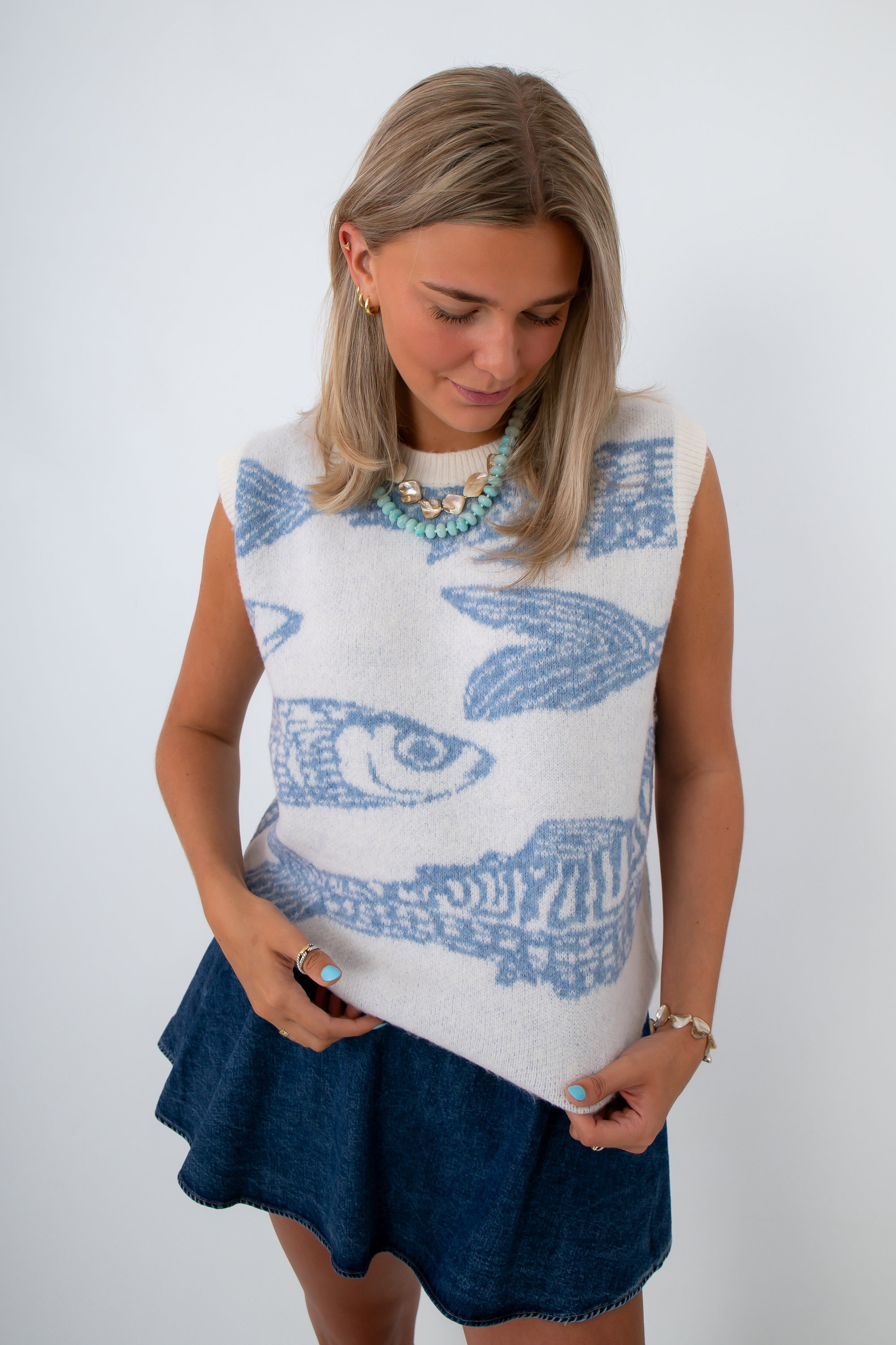 woman looking down wearing sleeveless knit fish sweater with blue fish pattern