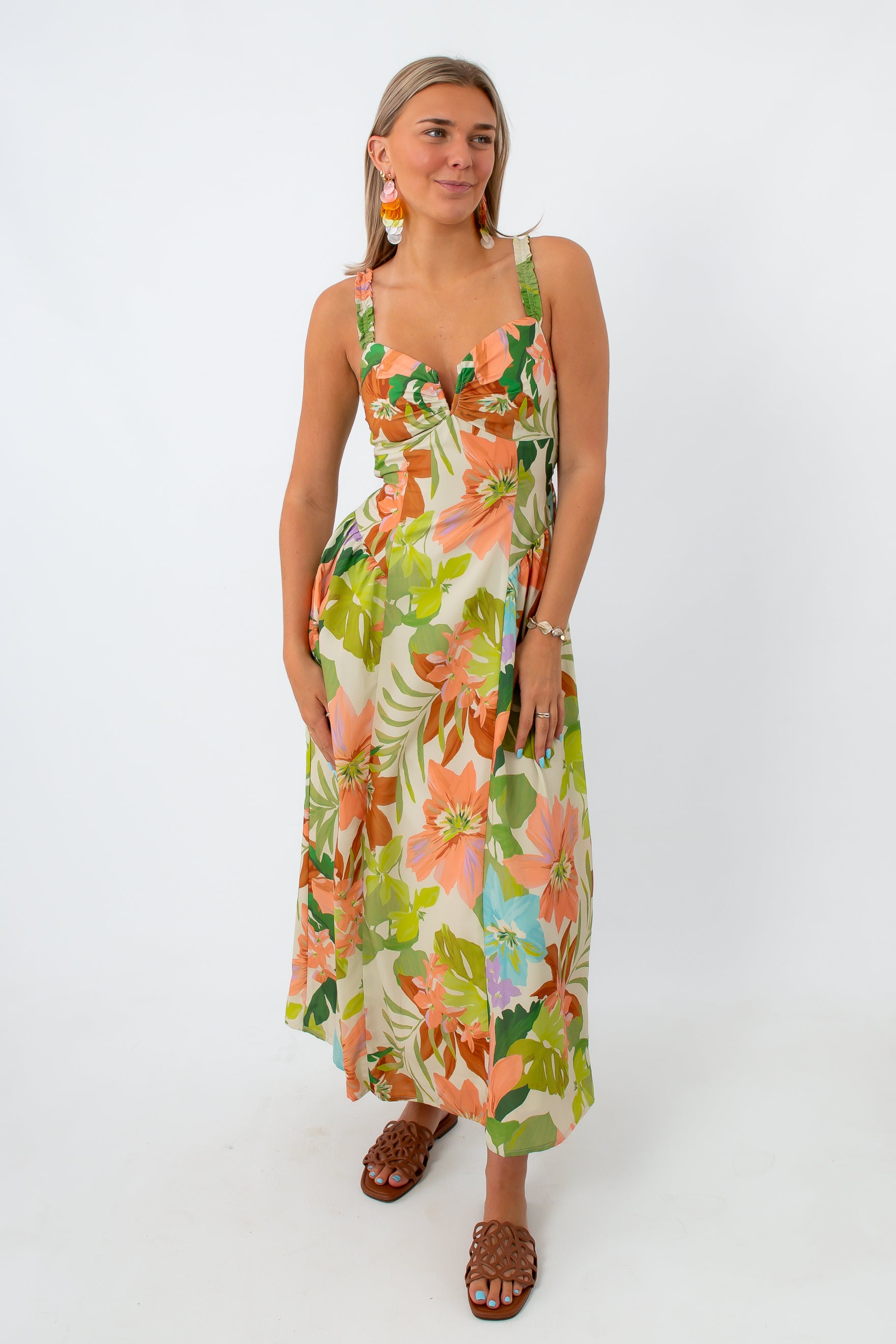 Woman in tropical floral maxi dress with colorful earrings and brown sandals