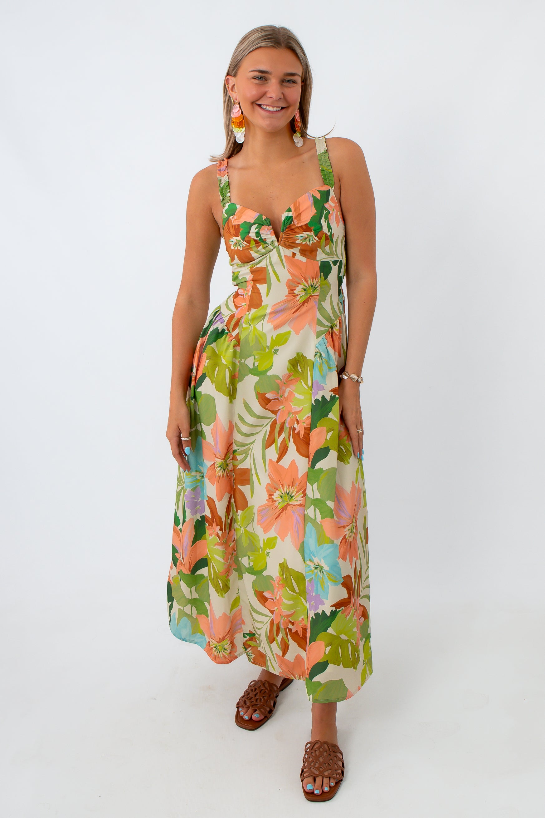 Woman in floral maxi dress with colorful earrings and brown sandals smiling